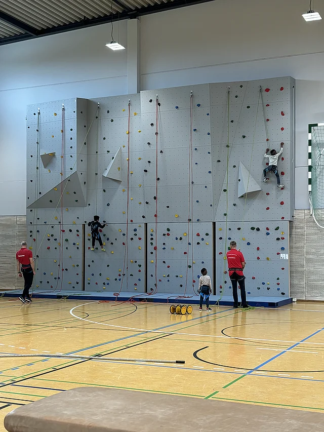 Klettern an der Kletterwand Kind klettert unter Aufsicht an der Kletterwand in der Allertalsporthalle